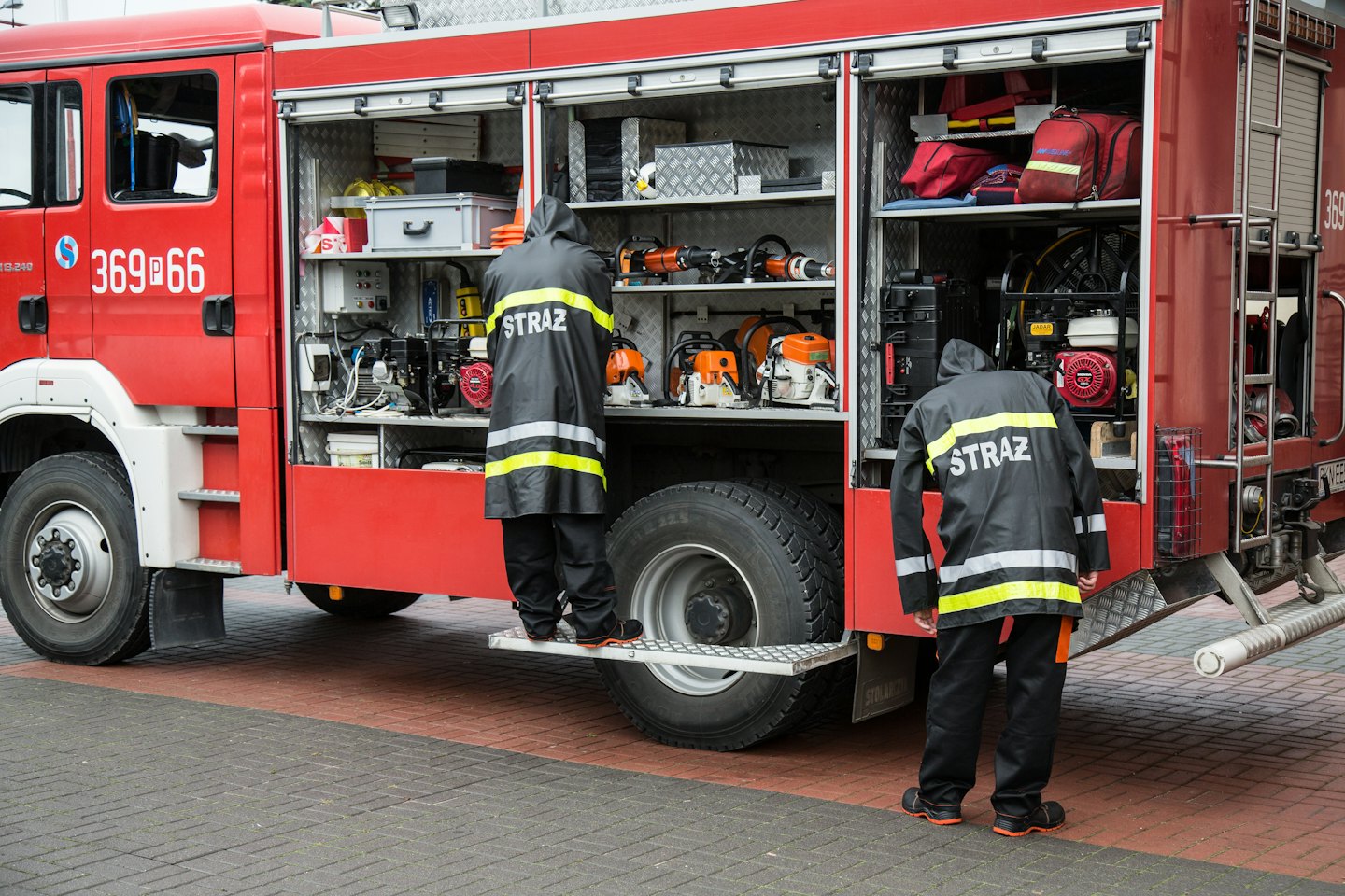 Firefighters accessing equipment from red fire truck side compartments.