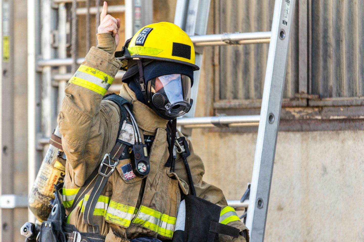 Firefighter in full gear points upwards with a gloved hand.